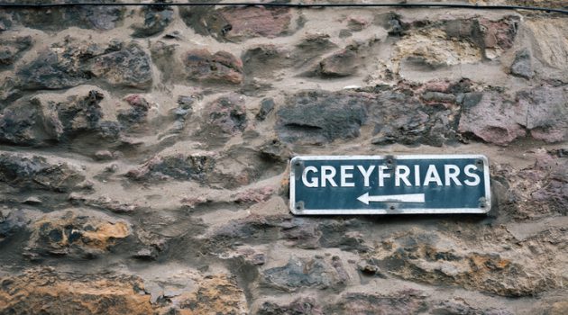 An old tourist direction sign on a stone wall in Edinburgh pointing to the Greyfriars Kirkyard.